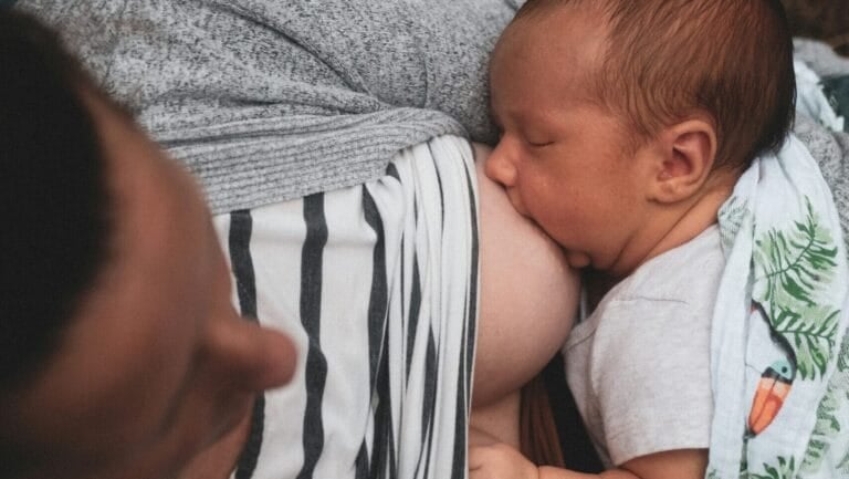 Baby breastfeeding at a mother’s chest, wrapped in a patterned blanket