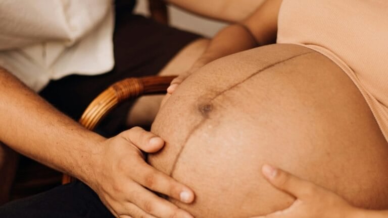 Hands cradling a pregnant belly with a visible linea nigra.